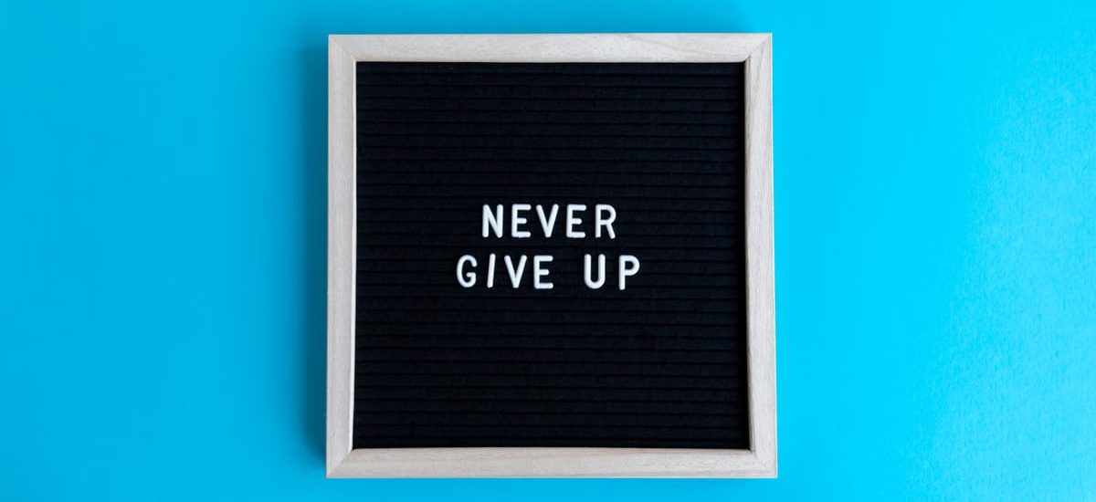 Black letter board with 'Never Give Up' message on a vibrant blue background.